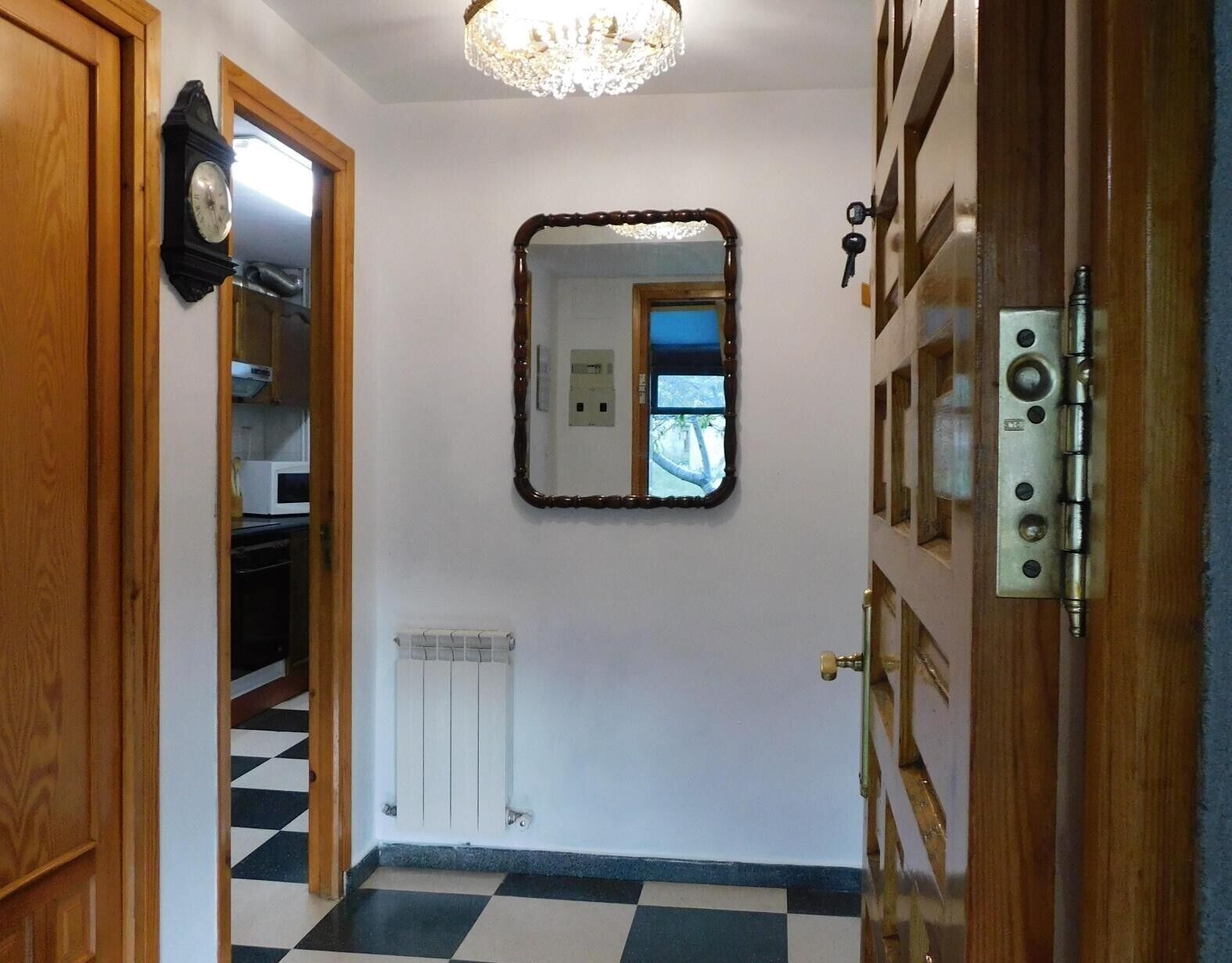 Un pasillo con piso a cuadros blanco y negro, una puerta de madera, un espejo en la pared y un radiador.