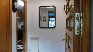 Un pasillo con piso a cuadros blanco y negro, una puerta de madera, un espejo en la pared y un radiador.