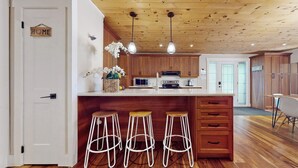 Una cucina moderna con mobili in legno, un'isola centrale con sgabelli, illuminazione a sospensione e vista sull'area pranzo adiacente.