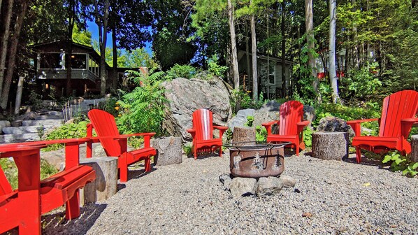 A gravel patio with red Adirondack chairs, a fire pit, and a rustic wooden structure in the background.