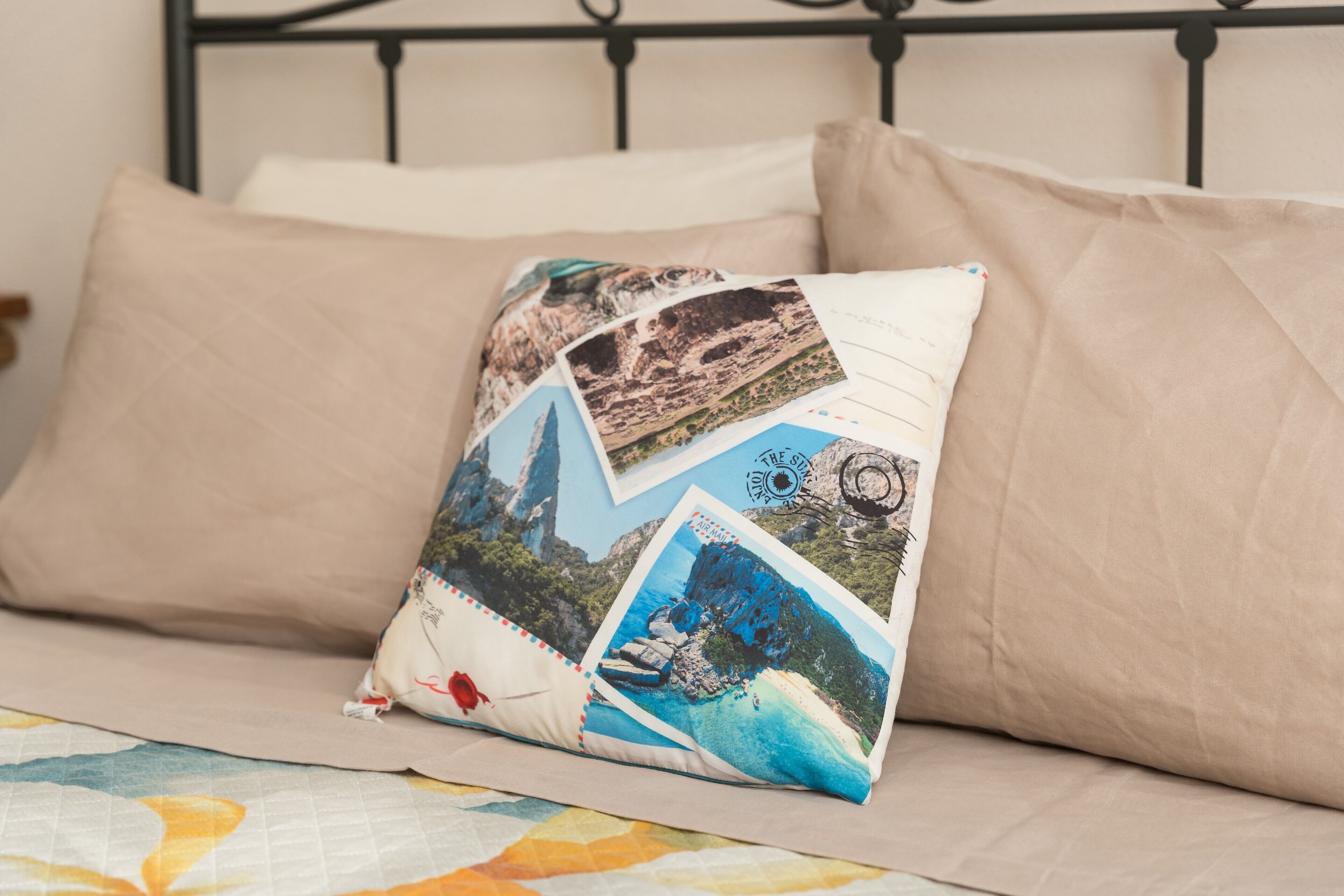 Ein Bett mit einer beigen Decke und Kissen, eines davon mit einer Collage aus Reisefotos.