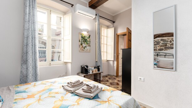 A bedroom with a bed, a desk, a mirror, and a view of a stone wall. - Studio 'Pistiddu' with Shared Garden, Wi-Fi, and Air Conditioning (Dorgali)