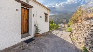 Un edificio blanco con puerta de madera, una planta en maceta y vistas a un paisaje montañoso.