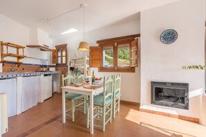 Eine Küche mit Esstisch, Stühlen, einer Pendelleuchte, einem Fenster und einem Kamin.