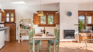 Una cocina con gabinetes de madera, una mesa de comedor con sillas, un lámpara colgante y una chimenea.