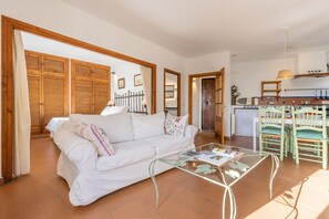 Ein Wohnzimmer mit einem weißen Sofa, einem Glastisch und einer Küchenzeile mit Holzschränken und einer gefliesten Spritzschutzwand.
