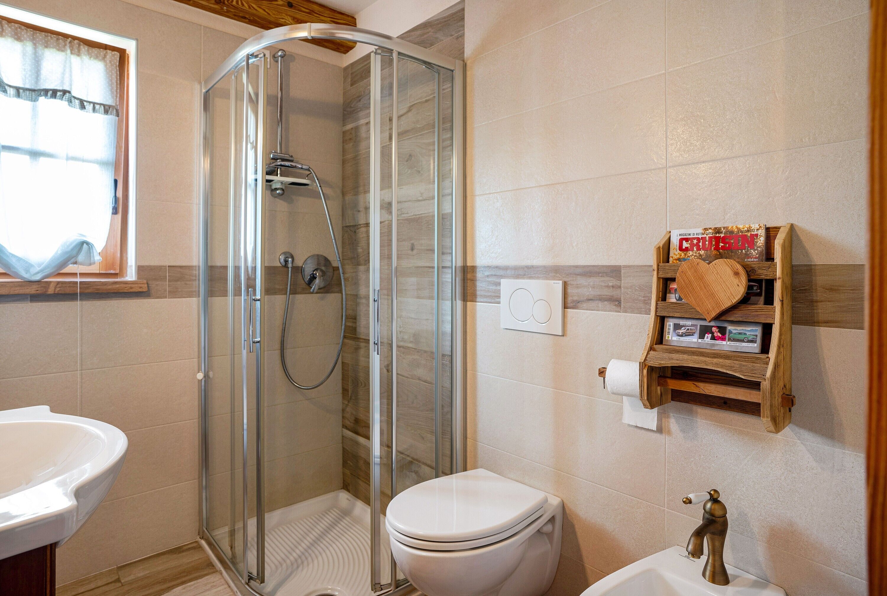Un baño con cabina de ducha de vidrio, inodoro blanco, lavamanos y estante de madera con un objeto con forma de corazón.