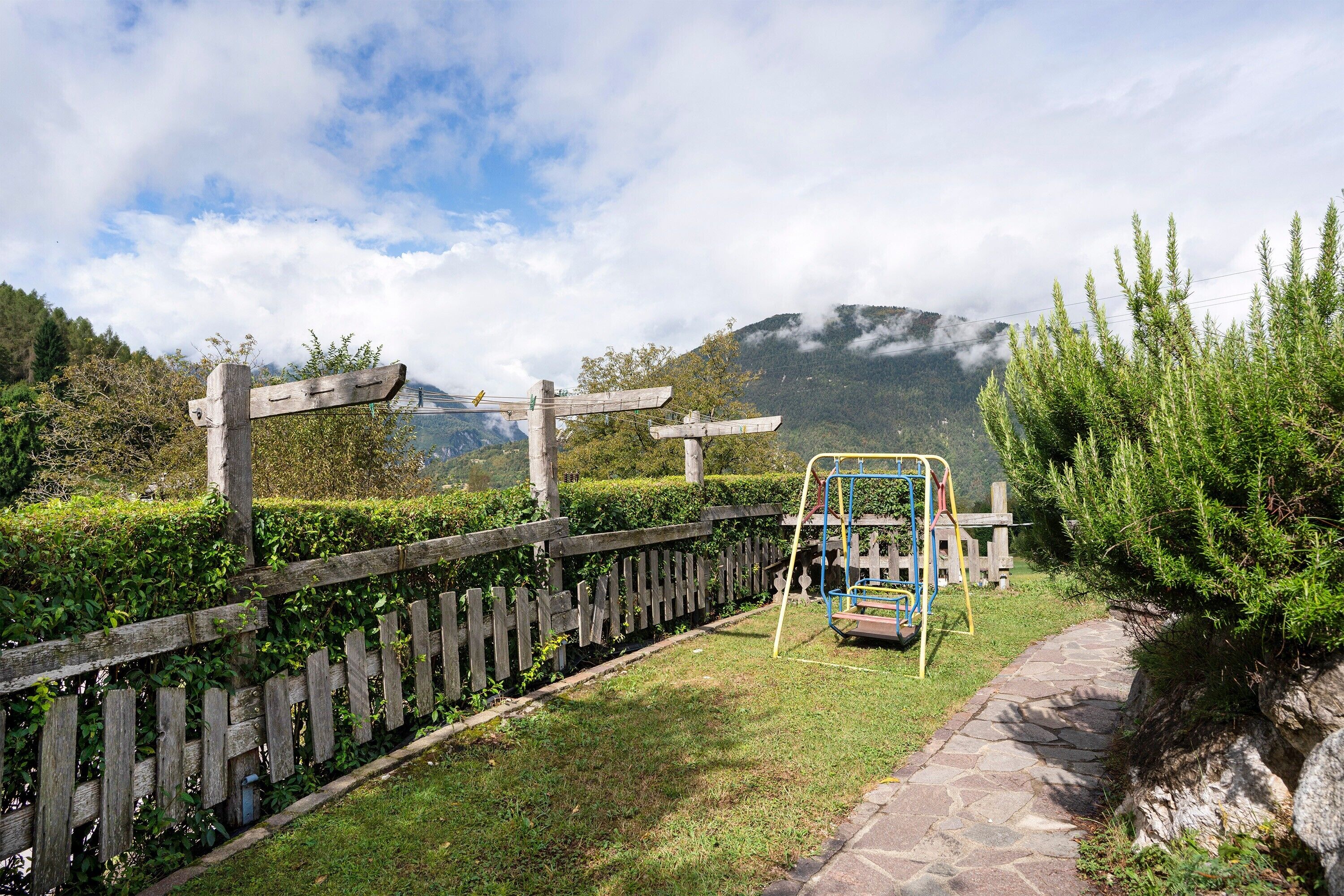 A wooden fence, a stone pathway, and a playground with a swing set.
