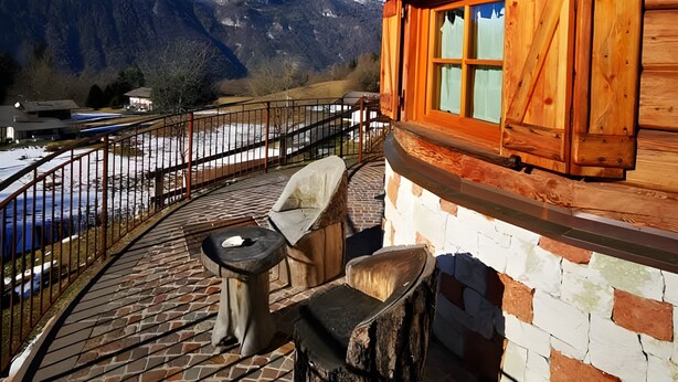 A wooden cabin with a stone patio, a view of mountains, and a fenced outdoor area. - Chalet 'Baita  Alabama' with Mountain View, Private Terrace and Wi-Fi (Arsiè)
