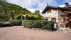 A stone building with a brick pathway leading to it, surrounded by a hedge and trees. - Chalet 'Baita  Alabama' with Mountain View, Private Terrace and Wi-Fi (Arsiè)