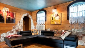 Interior em madeira com sofá modular, parede de pedra e obras de arte.