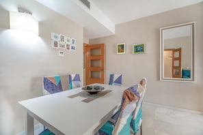 Un coin repas avec une table blanche, des chaises dotées de coussins à motifs, des tableaux encadrés accrochés au mur et un grand miroir.