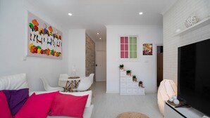 A modern living room with a white sofa, a flat-screen TV, and a dining area with a small table and chairs.