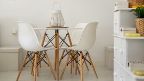 A dining area with a white table, two white chairs, a white lantern, and a white cabinet with drawers.