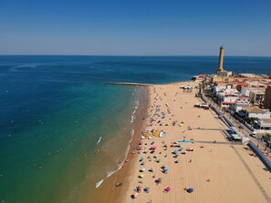An aerial view of a beach with a lighthouse, beach umbrellas, and a promenade with buildings. - Apartment 'Casa Margara' with Wi-Fi and Air Conditioning (Chipiona)