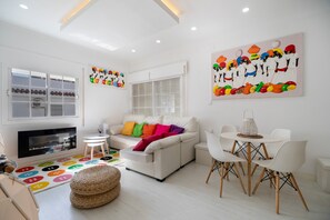 Ein modernes Wohnzimmer mit einer Couch, Sesseln, einem Kamin und farbenfroher Kunst.