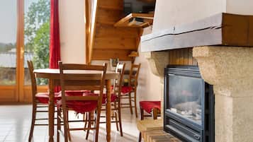 A room with a fireplace, wooden chairs, and a dining table.