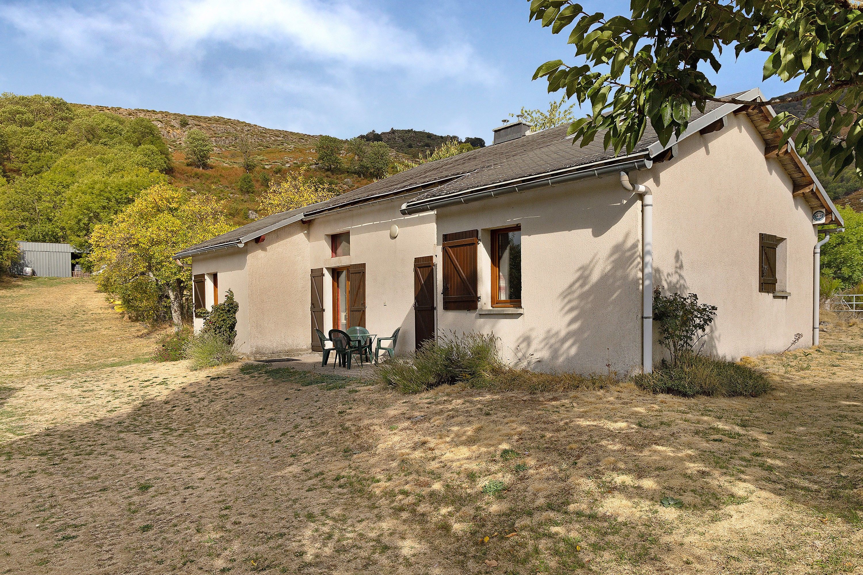 A single-story house with a sloped roof, a small porch with chairs, and a clear sky.