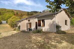 A single-story house with a sloped roof, a small porch with chairs, and a clear sky. - Cottage 'Gite Saint Guiral' with Mountain View, Private Terrace and Private Garden (Dourbies)