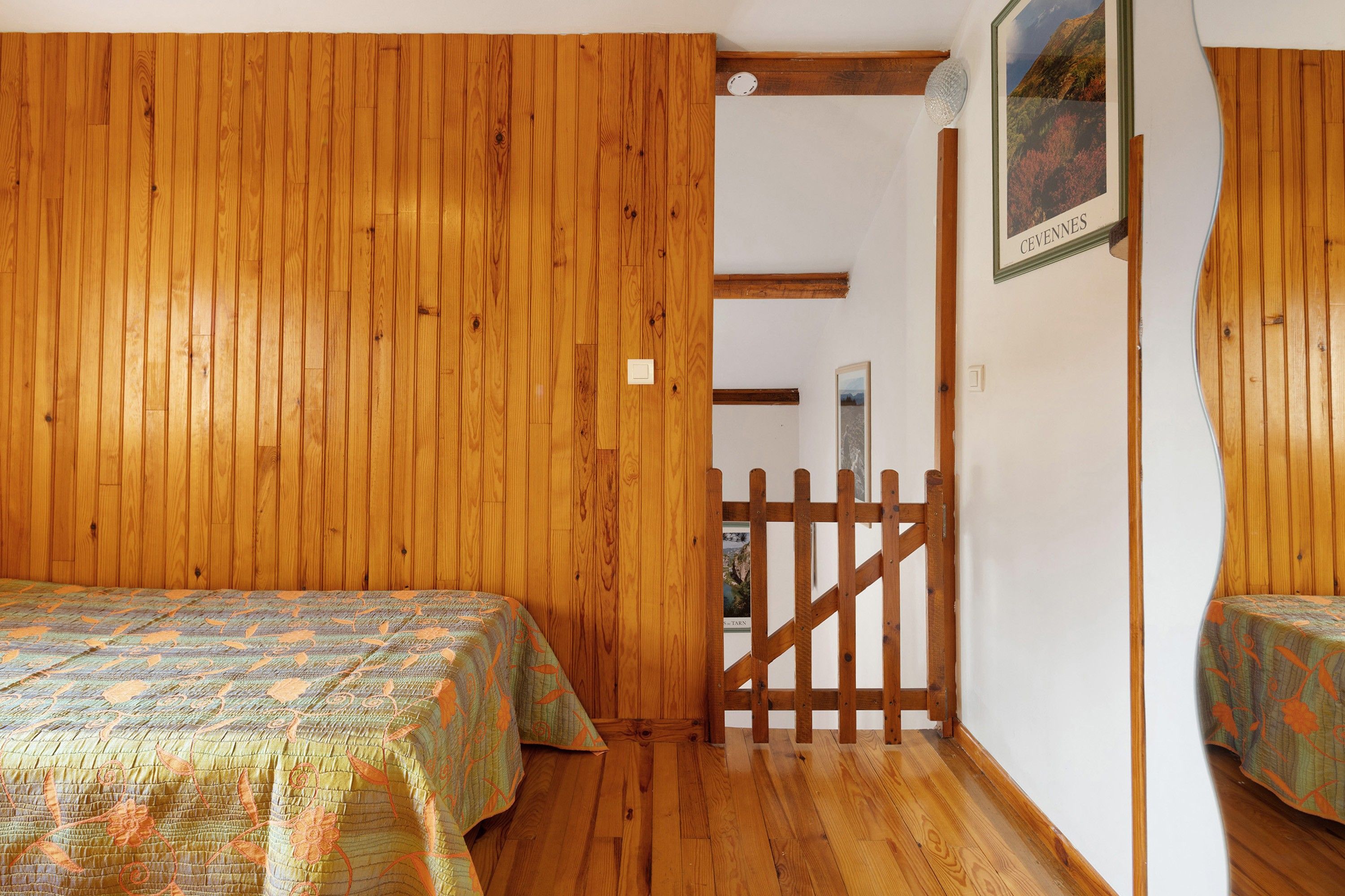 Ein Zimmer mit Holzwänden und Holzböden, zwei Betten mit gemusterten Betttextilien, ein hölzernes Tor und ein gerahmtes Bild an der Wand.