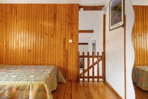 A room with wooden walls and floors, two beds with patterned bedding, a wooden gate, and a framed picture on the wall. - Cottage 'Gite Saint Guiral' with Mountain View, Private Terrace and Private Garden (Dourbies)