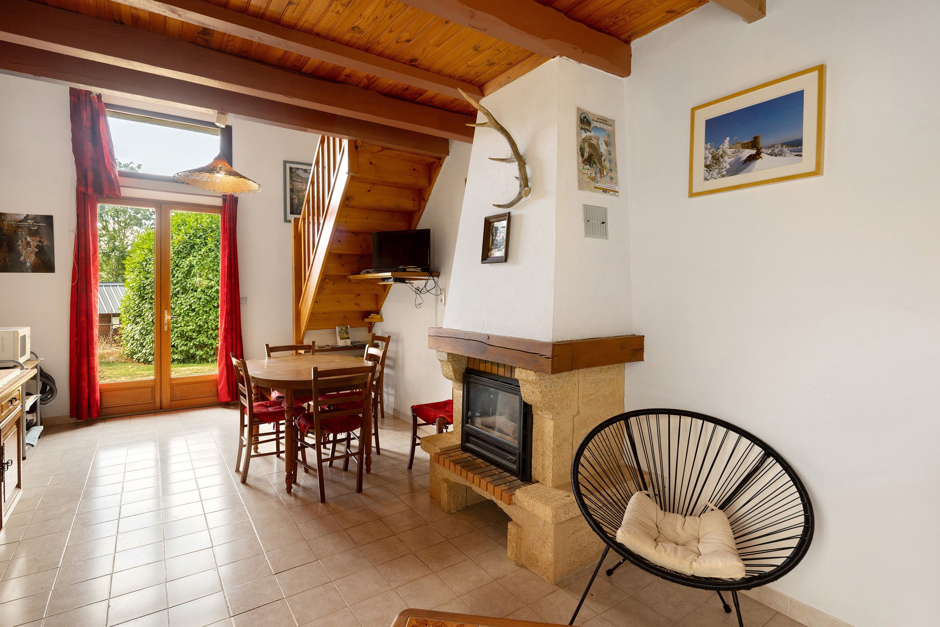 Une pièce chaleureuse avec une cheminée, des poutres apparentes en bois au plafond, une table à manger avec des chaises et un téléviseur.