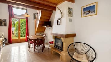 A cozy room with a fireplace, wooden ceiling beams, a dining table with chairs, and a television.
