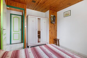 A room with a wooden ceiling, a white wardrobe, a green door, a patterned rug, and a small wooden stool. - Cottage 'Gite Saint Guiral' with Mountain View, Private Terrace and Private Garden (Dourbies)