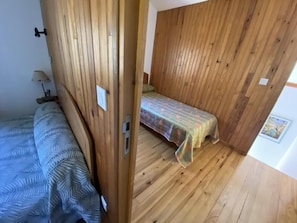 A room with wooden walls, a bed with a patterned bedspread, a small table with a lamp, and a framed picture on the wall. - Cottage 'Gite Saint Guiral' with Mountain View, Private Terrace and Private Garden (Dourbies)