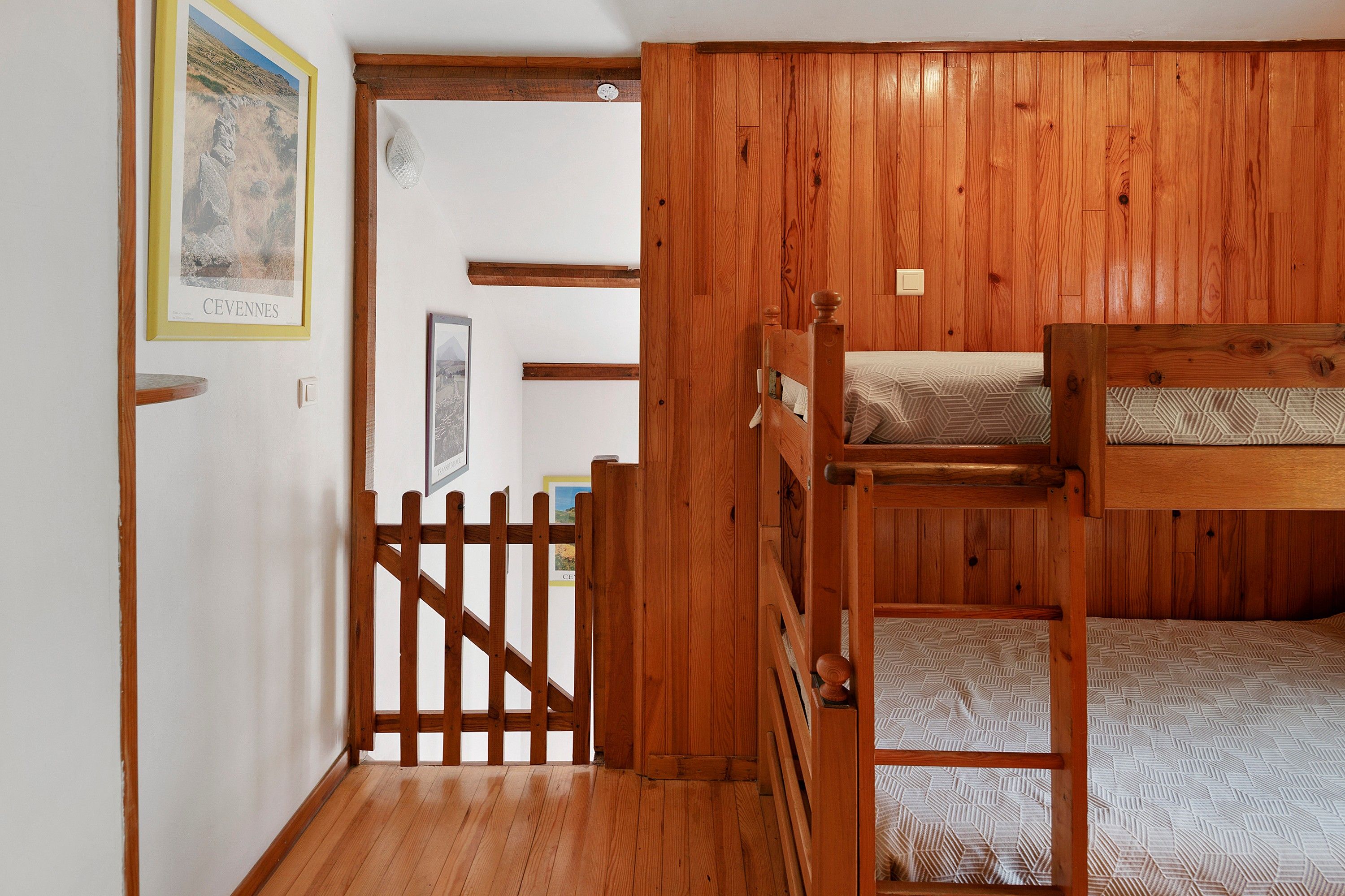 A room with wooden walls, a bunk bed, a door with a wooden gate, and a framed picture on the wall.
