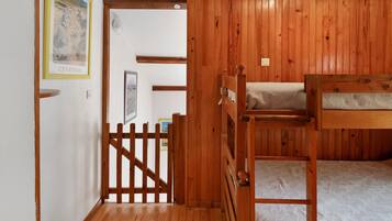 A room with wooden walls, a bunk bed, a door with a wooden gate, and a framed picture on the wall.