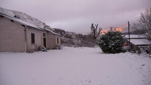A snow-covered rural scene with a building, a bush, and a distant sunset. - Holiday Home 'Gîte Le Suquet' with Mountain View and Private Terrace (Dourbies)