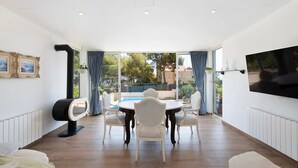 Una sala de estar moderna con comedor, un televisor montado en la pared y vistas al exterior.