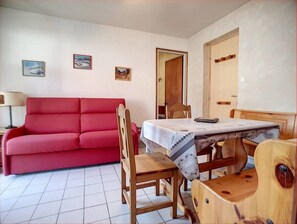 A room with a red sofa, wooden dining table, chairs, and a door. - Apartment 'Apt Le Retour Aux Neiges - Les Gets' with Mountain View, Balcony and Wi-Fi (Les Gets)