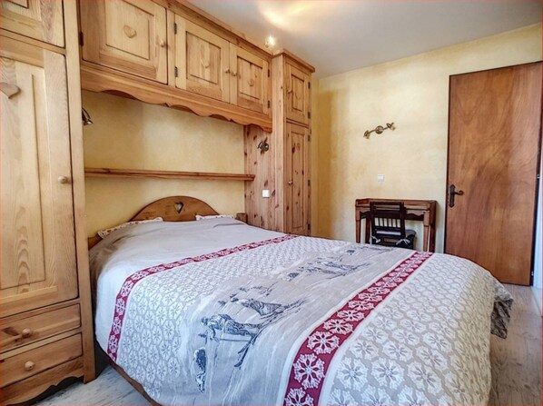 Quarto com cama, guarda-roupa de madeira e uma mesinha.