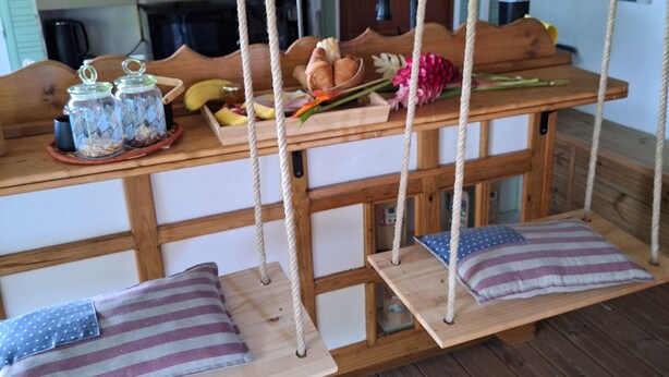 Un rústico comedor de madera con un columpio de cuerda colgante, bancos de madera y una mesa de madera con diversos alimentos y elementos decorativos.