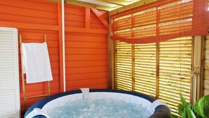 Una bañera caliente interior con exterior inflable azul y blanco, frente a una pared roja con persianas de madera y una toalla blanca colgada en un perchero de madera.
