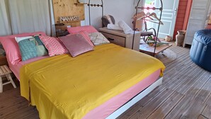 Un dormitorio con cama, almohadas, cabecera de madera, mesita de noche, una silla y un perchero.