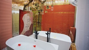 Un baño con dos tinas blancas, pared de azulejos rojos y techo de paja.
