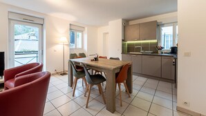 A modern kitchen with a dining area, featuring a wooden table and chairs, a kitchen island, and a view of the outside.