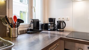 A kitchen with a toaster, coffee maker, and kettle on the counter, near a window with a view of a building.