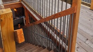 A wooden deck with a metal railing, a brick building, and a view of a parking area and trees. - Charming 3-bedroom historic Brick Loft in Uniontown with WiFi (Uniontown)