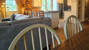 A cozy living room with a sofa, dining table, and chairs, a kitchen with white cabinets, and a brick wall. - Charming 3-bedroom historic Brick Loft in Uniontown with WiFi (Uniontown)