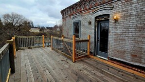 A wooden deck with a metal railing, a brick wall, and a black door with a window. - Charming 3-bedroom historic Brick Loft in Uniontown with WiFi (Uniontown)