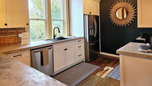 A modern kitchen with white cabinets, a stainless steel refrigerator, a large window, and a sunburst mirror on the wall. - Charming 3-bedroom historic Brick Loft in Uniontown with WiFi (Uniontown)