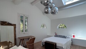 Un dormitorio con cama, una silla, una mesa, un ventanal y un espejo.