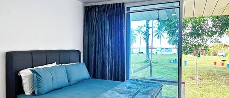 A bedroom with a bed, a window with curtains, and a view of a grassy area with trees and a building.