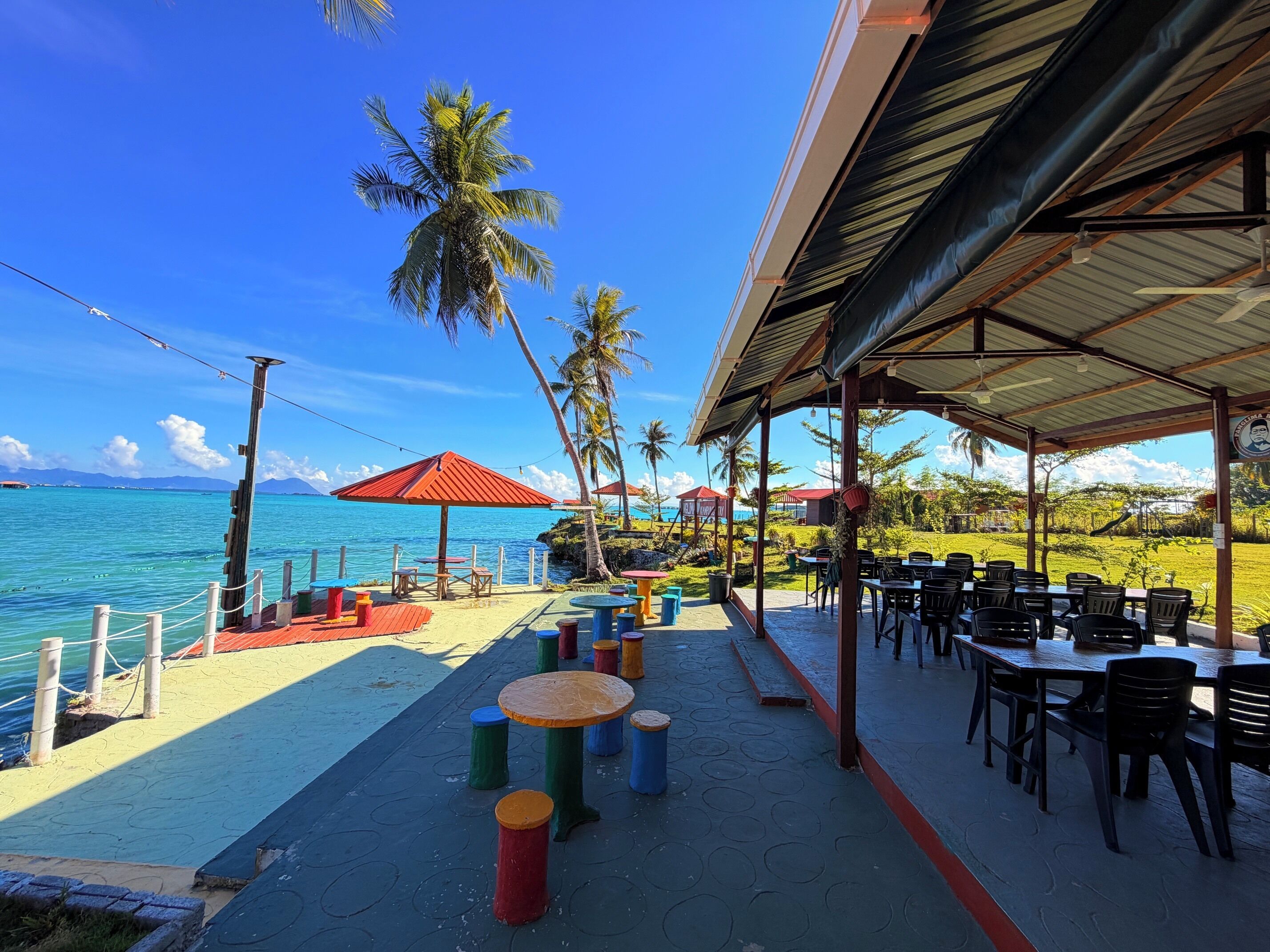 Un restaurant en bord de mer avec une terrasse, des palmiers et une vue sur l’océan.