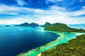 Una isla tropical con aguas turquesas cristalinas, exuberante vegetación y algunos edificios pequeños cerca de la costa.