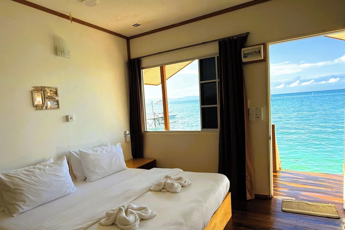Una habitación de hotel con una cama, un ventanal con vista al mar y piso de madera.